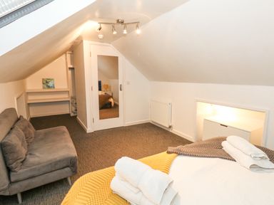 A bedroom with a bed and folded towels a gray sofa a wall mirror and a radiator at Beachaven in Weymouth