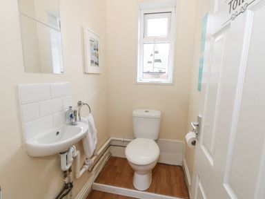 A small toilet room with a white toilet a sink with a towel a mirror a window and a small decorative boat on the windowsill at Beachaven in Weymouth
