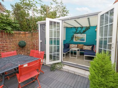 An outdoor patio area with a black table and red chairs next to a room with blue walls and blue cushioned seating at Beachaven in Weymouth