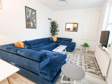 A living room with a blue sectional sofa yellow pillows two round tables and a wall-mounted tv at Beachaven in Weymouth
