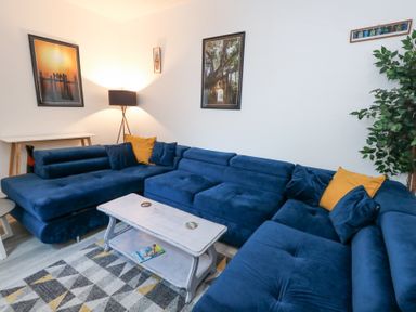 A living room with a blue sectional sofa and yellow pillows a white coffee table and a floor lamp at Beachaven in Weymouth