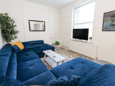 A living room with blue sectional sofa a coffee table a flat screen TV and a large window at Beachaven in Weymouth