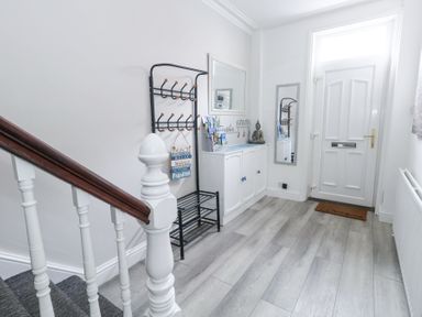An entryway with a white door a black coat rack a white cabinet with a statue and brochures a staircase with white spindles and brown handrail at Beachaven in Weymouth