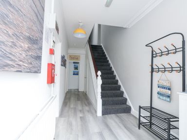 A hallway with stairs carpeted in dark fabric a black coat rack and wall art at Beachaven in Weymouth
