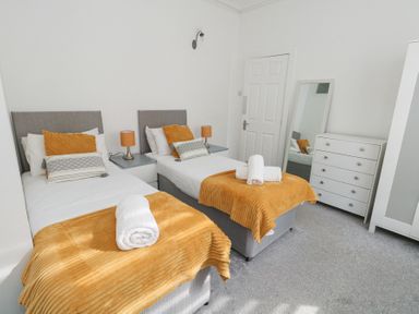 A bedroom with two single beds side by side each with orange blankets and pillows beside a white chest of drawers and a full-length mirror at Beachaven in Weymouth