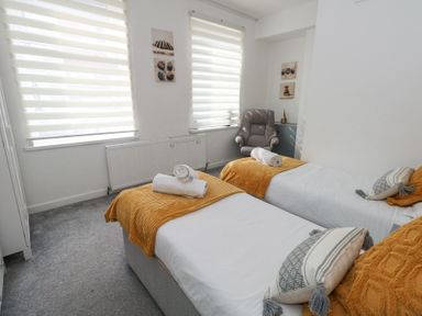 A bedroom with two single beds each with a white sheet and mustard throw at Beachaven in Weymouth