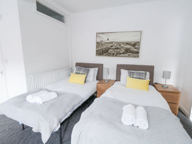 A bedroom with two single beds with pillows and rolled towels and wooden nightstands with lamps at Beachaven in Weymouth