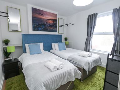 A bedroom with two single beds a blue headboard green lamps and a large window at Beachaven in Weymouth