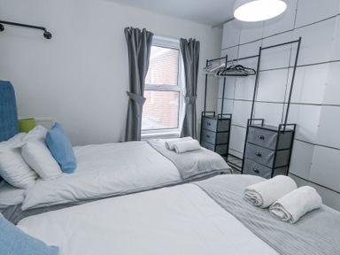 A bedroom with two single beds gray curtains and open closet storage at Beachaven in Weymouth