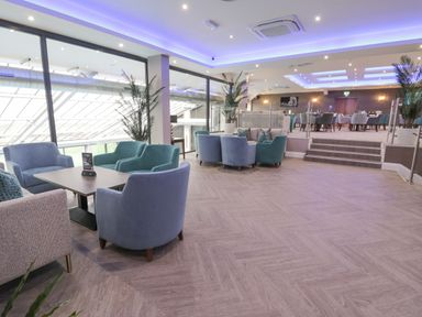 A large lounge area with chairs and tables and plants near glass windows at Classic Lodge 25 in Dyserth