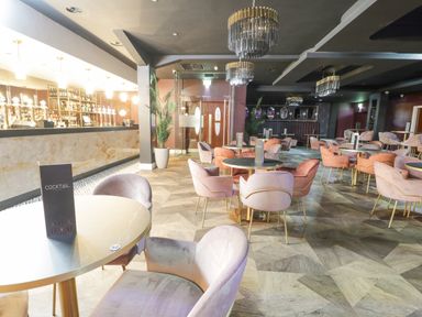 An empty cocktail bar with multiple round tables and upholstered chairs with a bar counter and chandeliers at Classic Lodge 25 in Dyserth