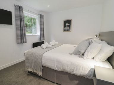 A bedroom with a bed made with white linens and gray pillows next to a window with gray curtains at Classic Lodge 25 in Dyserth