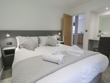 A bedroom with a double bed white linens and decorative pillows a wooden door an open doorway and a desk with a chair at Classic Lodge 25 in Dyserth