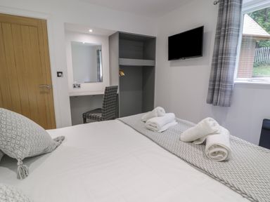 A bedroom with a bed towels a chair a desk a wall mounted tv and a window with curtains at Classic Lodge 25 in Dyserth