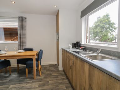 A kitchen with wooden cabinets a sink and a dining table with blue chairs at Classic Lodge 25 in Dyserth