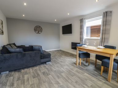 A living room with a dark sofa a wooden dining table with chairs and a wall mounted tv at Classic Lodge 25 in Dyserth
