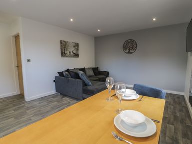 A dining table set with plates bowls and glasses next to a gray sofa in a living room at Classic Lodge 25 in Dyserth