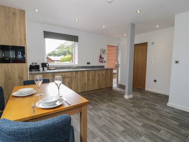 A kitchen with wooden cabinets a dining table set for two and a door open to outside at Classic Lodge 25 in Dyserth