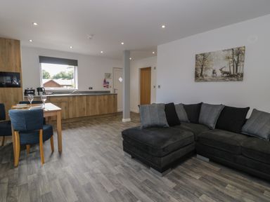 An open plan kitchen and living area with a black sofa and wooden dining table at Classic Lodge 25 in Dyserth