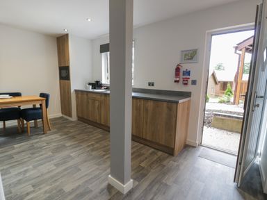 A kitchen with wooden cabinets a dining table with chairs and an open door showing outside at Classic Lodge 25 in Dyserth