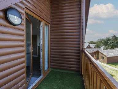 A balcony with artificial grass and wooden railing outside a wooden cabin at Premier Lodge 41 in Dyserth