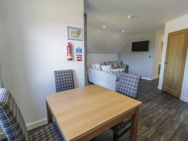 A dining area with a wooden table and four plaid chairs next to a living room with a gray sofa and a wall-mounted TV at Premier Lodge 41 in Dyserth