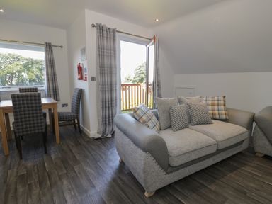 A living area with a sofa, dining table with chairs, and an open door leading to a balcony at Premier Lodge 41 in Dyserth