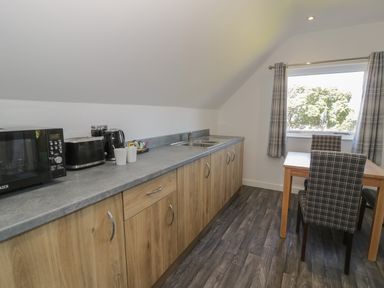A kitchen with wooden cabinets a microwave toaster kettle mugs a sink and a table with two chairs near a window with curtains at Premier Lodge 41 in Dyserth