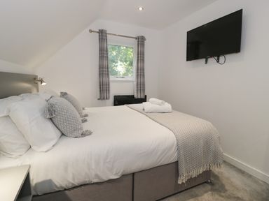 A bedroom with a bed with pillows and a blanket beside a window with curtains and a wall mounted television at Premier Lodge 41 in Dyserth