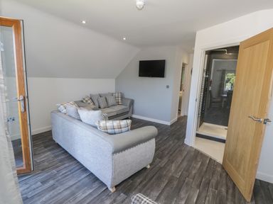 A living room with two sofas a wall-mounted TV and an open door leading to a shower at Premier Lodge 41 in Dyserth