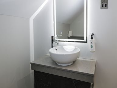 A bathroom sink with a round white basin faucet a lit square mirror and a hand wash dispenser on the wall at Premier Lodge 41 in Dyserth