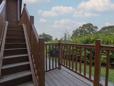 Wooden staircase and deck with railing overlooking a green garden with trees at Premier Lodge 41 in Dyserth