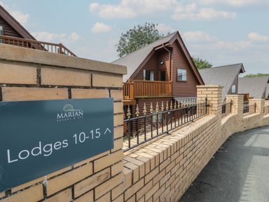 A brick wall with a sign indicating lodges 10-15 and wooden lodges behind the wall at Classic Lodge 15 in Dyserth