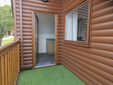 A balcony with artificial grass and wooden railing outside a lodge with an open door showing a kitchenette at Classic Lodge 15 in Dyserth