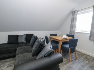 A living room with a black sofa and a wooden dining table with blue chairs near a window at Classic Lodge 15 in Dyserth