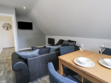 A living room with a wooden dining table set with bowls and glasses and a dark sofa with cushions and a wall-mounted TV at Classic Lodge 15 in Dyserth