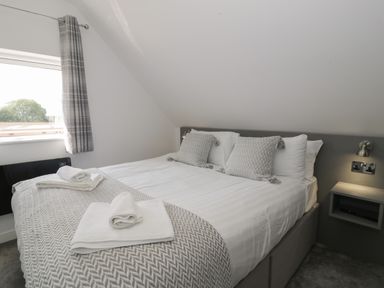 A bedroom with a double bed with patterned pillows and folded towels near a window with plaid curtains at Classic Lodge 15 in Dyserth
