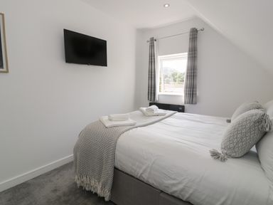 A bedroom with a bed with pillows and folded towels a window with curtains and a mounted television on the wall at Classic Lodge 15 in Dyserth