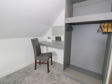 A corner with a gray desk and a checkered chair next to an open closet with hangers at Classic Lodge 15 in Dyserth
