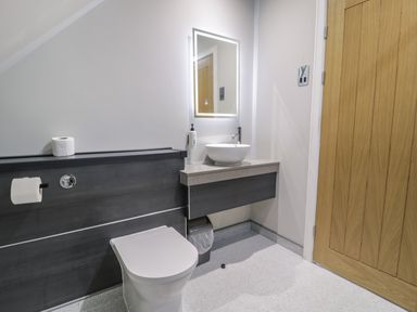A bathroom with a toilet sink counter illuminated mirror wooden door and toilet paper holder at Classic Lodge 15 in Dyserth