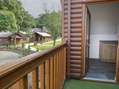 A view from a wooden balcony overlooking cabins and trees at Classic Lodge 15 in Dyserth