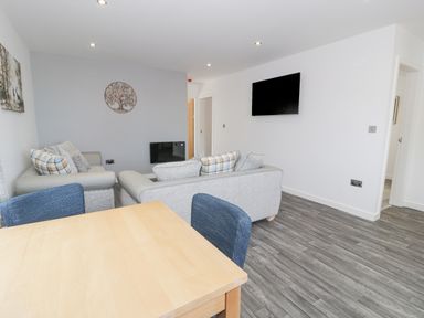 A living room with two sofas a wooden dining table with blue chairs a wall-mounted TV and wall art at Luxury Lodge 46 in Dyserth