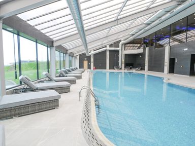 An indoor pool with lounge chairs along the side and large windows at Luxury Lodge 46 in Dyserth