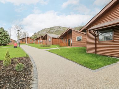 A pathway between wooden lodges with grass and trees and hills in the background at Luxury Lodge 46 in Dyserth
