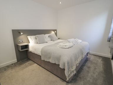 A bedroom with a double bed two pillows folded towels wall lamps and a window with curtains at Luxury Lodge 46 in Dyserth
