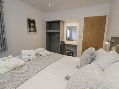 A bedroom with a made bed with towels and bathrobes on it a chair at a desk with a mirror an open closet a wooden door and a framed picture on the wall at Luxury Lodge 46 Dyserth