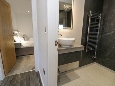 A bathroom with a sink and towel radiator next to a bedroom with a bed and pillows at Luxury Lodge 46 in Dyserth