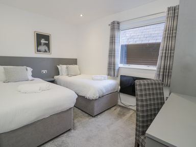 A bedroom with two single beds a window with curtains and a desk with a chair at Luxury Lodge 46 in Dyserth