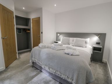 A bedroom with a bed with folded towels and robes two wooden doors and an open closet at Luxury Lodge 46 in Dyserth
