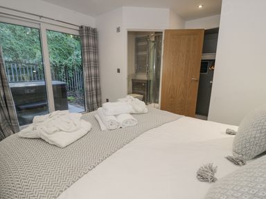 A bedroom with a bed with towels and bathrobes on it a door open to a bathroom and a glass door leading outside at Luxury Lodge 46 in Dyserth